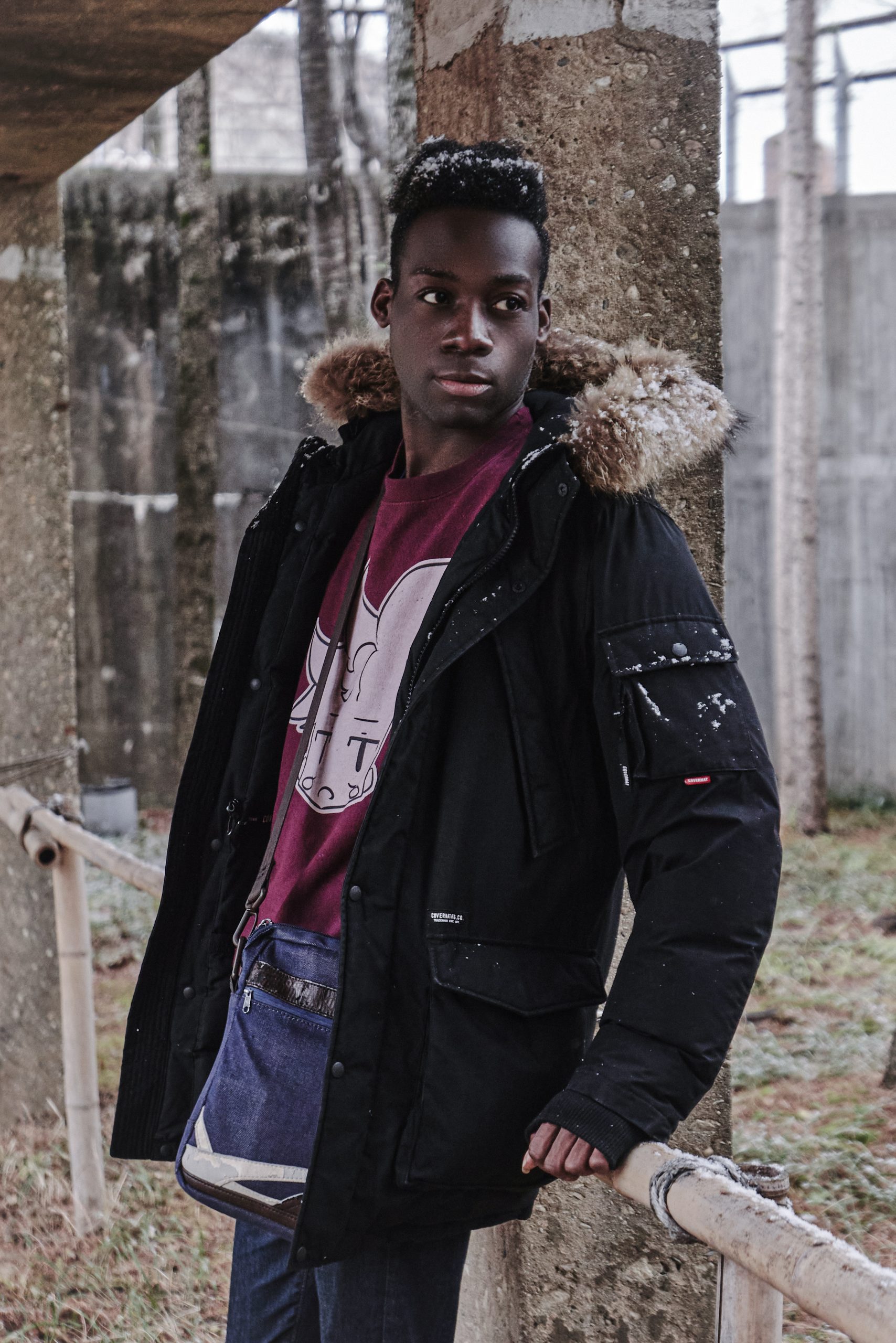 Sweat Jared Bordeaux - Look décontracté d’hiver | Philis Corp. Shop Adam appuyé contre un pilier, portant le sweat Jared bordeaux Philis Corp. Shop, reflet du calme et du froid hivernal.